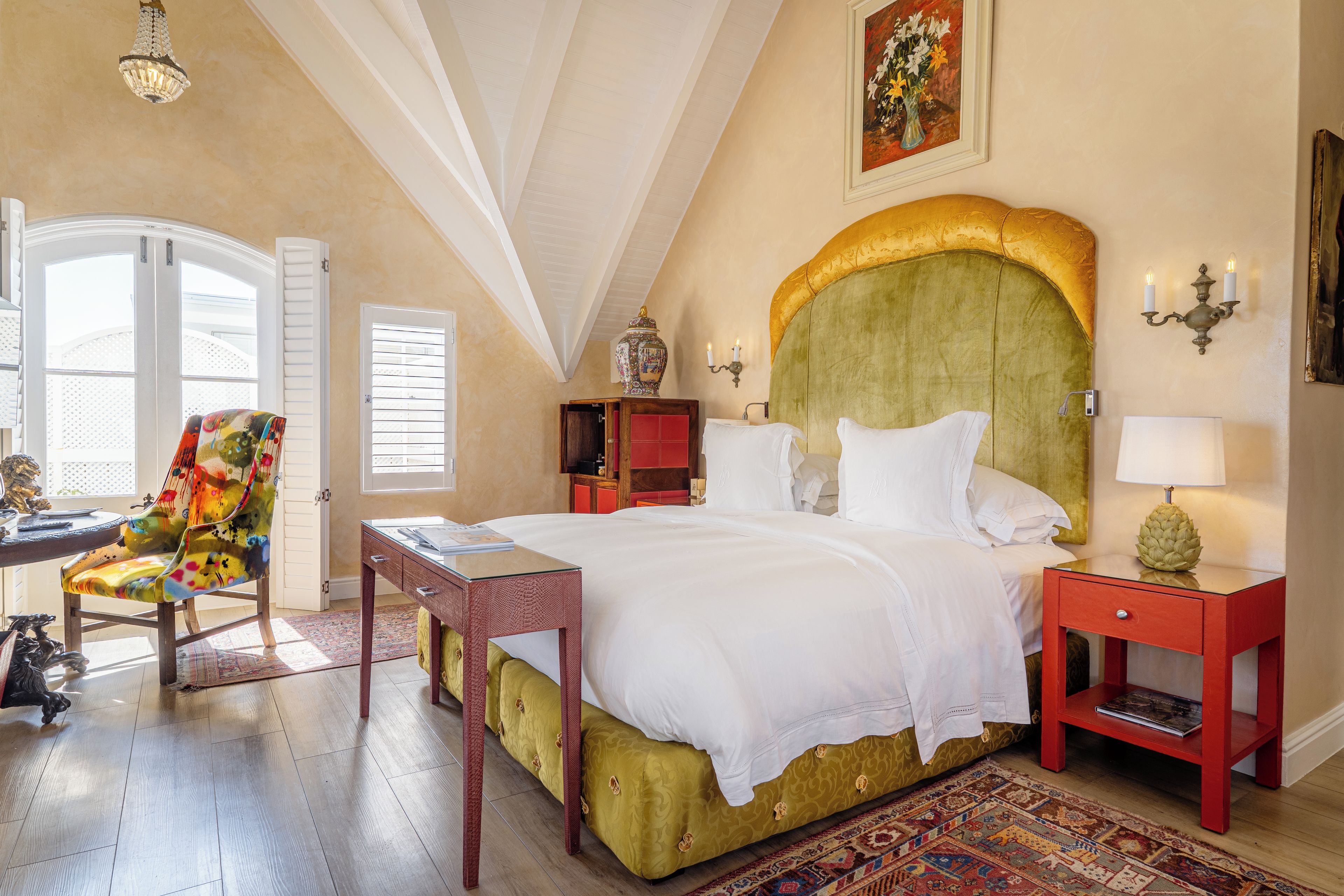 A bedroom with a large bed, a chair, a bedside table, a lamp, and a painting on the wall.