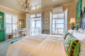 A spacious bedroom with a large bed, a desk with a chair, and a view through open shutters.