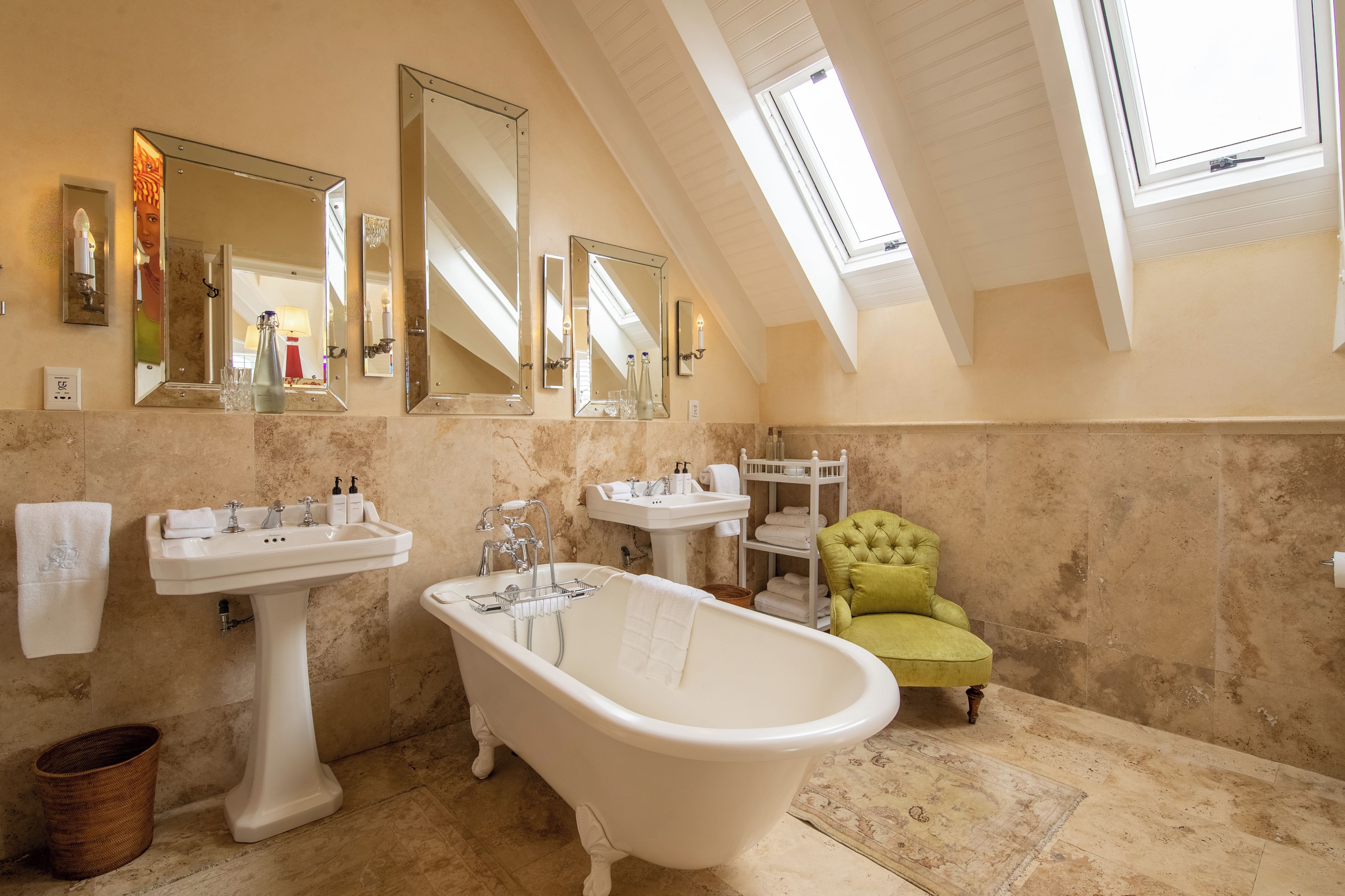 A bathroom with a freestanding bathtub, two sinks, a vanity, and a green armchair.