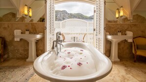 A luxurious bathroom with a large bathtub, two sinks, and a view of mountains through an open doorway. - Birkenhead House (Hermanus)