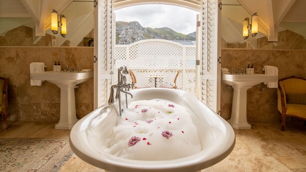 Ein luxuriöses Badezimmer mit einer großen Badewanne, zwei Waschbecken und Bergblick durch eine offene Tür.