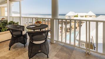Ein Balkon mit Korbmöbeln und einem Tisch mit Früchten, mit Blick auf Strand und Poolbereich.
