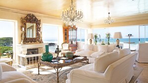 A spacious living room with a fireplace, white furniture, and a view of the ocean. - Birkenhead House (Hermanus)