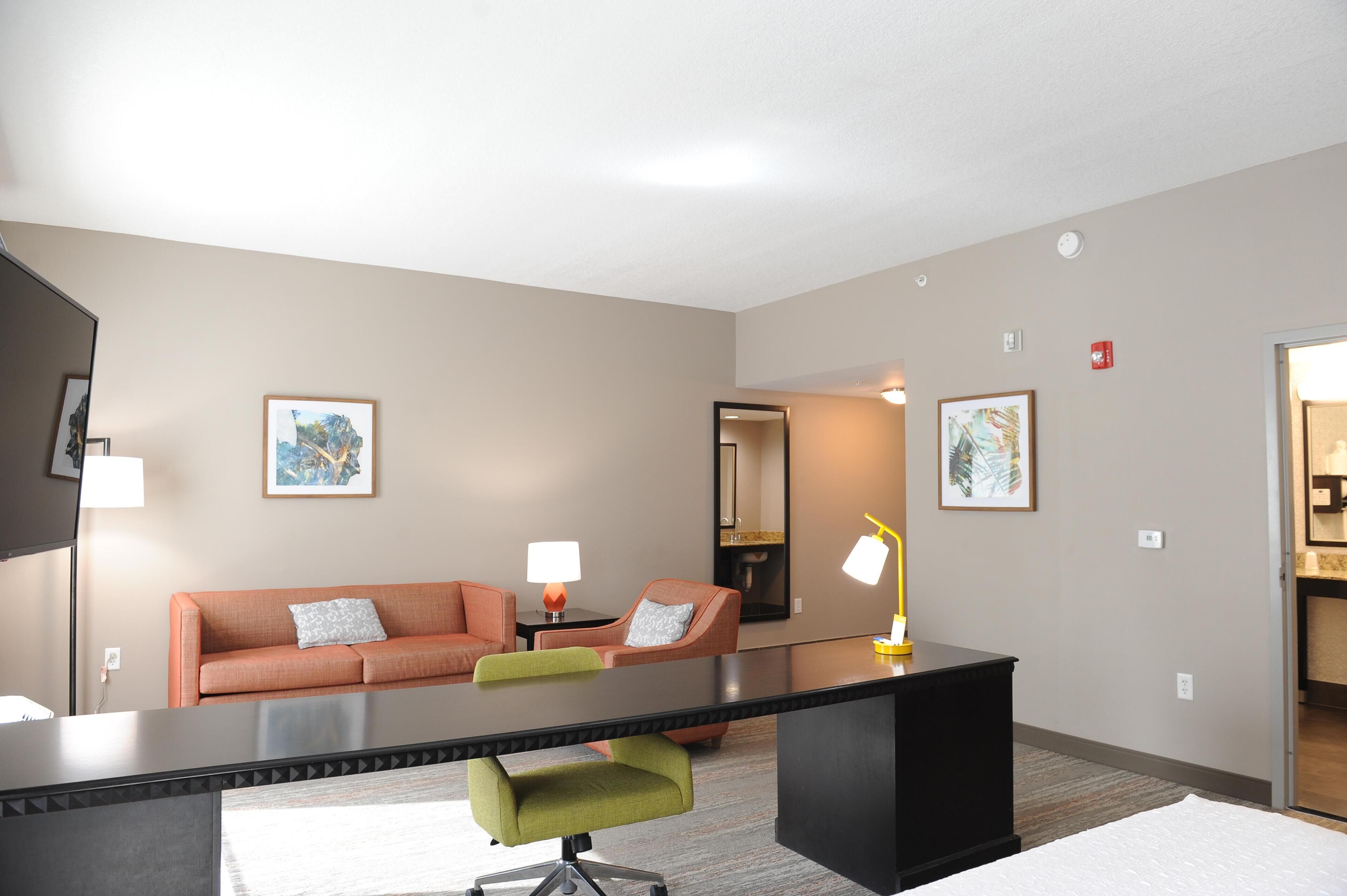 A hotel room with a large desk, two chairs, a sofa, and two lamps.