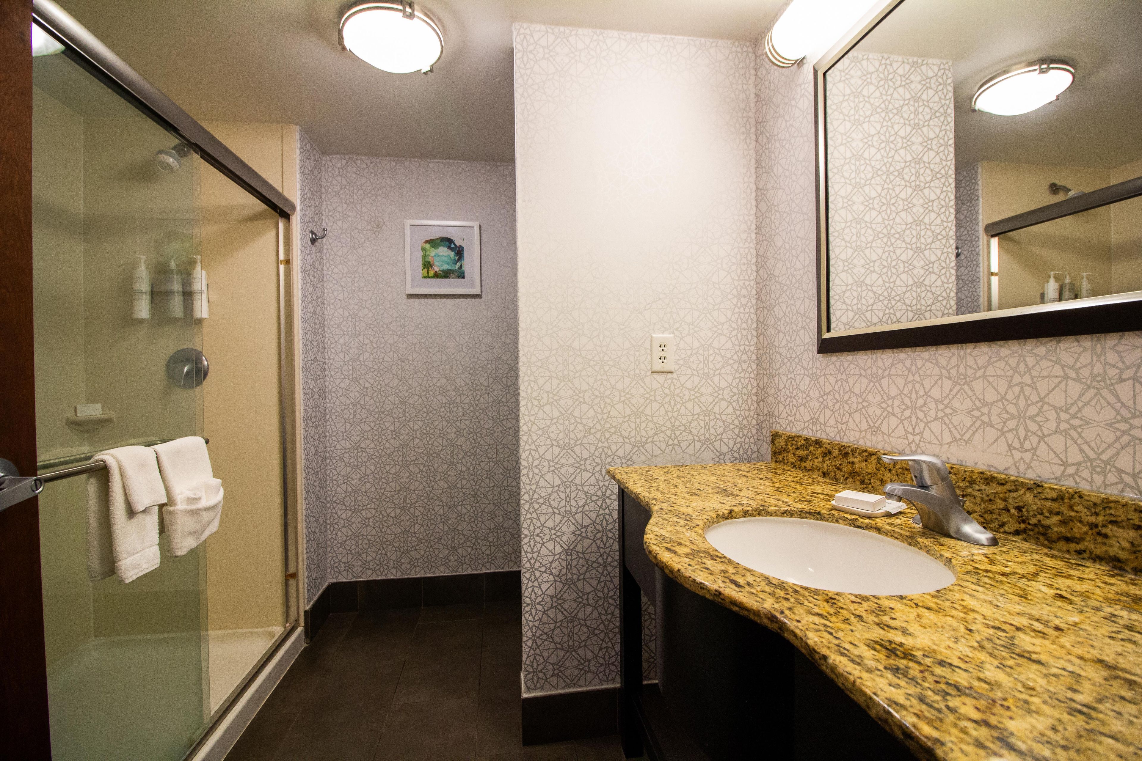 A bathroom with a glass shower enclosure, a sink with a granite countertop, and a mirror above the sink.
