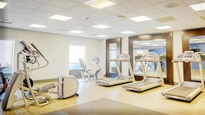 A fitness center with treadmills, elliptical machines, and a mirrored wall.