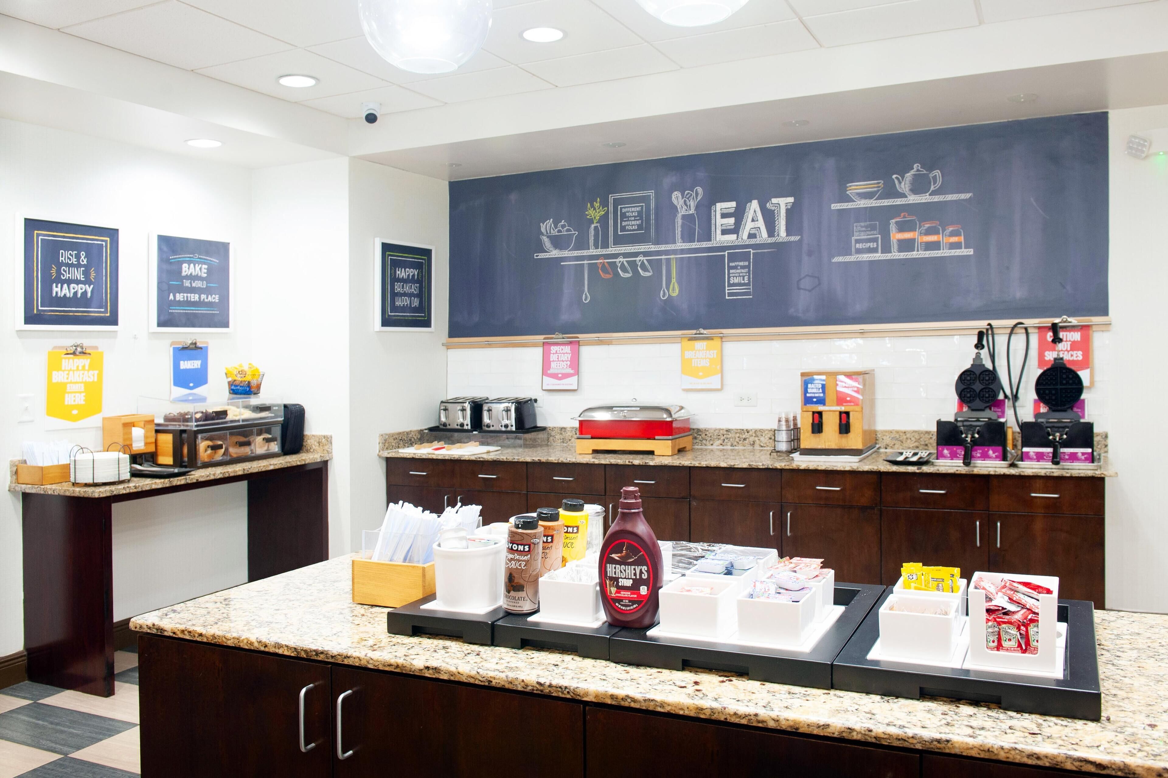Un comptoir-repas avec un tableau noir servant de panneau, des machines à café et divers produits alimentaires.