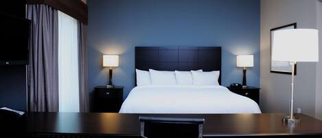 Quarto de hotel com uma cama grande, duas luminárias de cabeceira, uma escrivaninha com cadeira e uma televisão à esquerda.