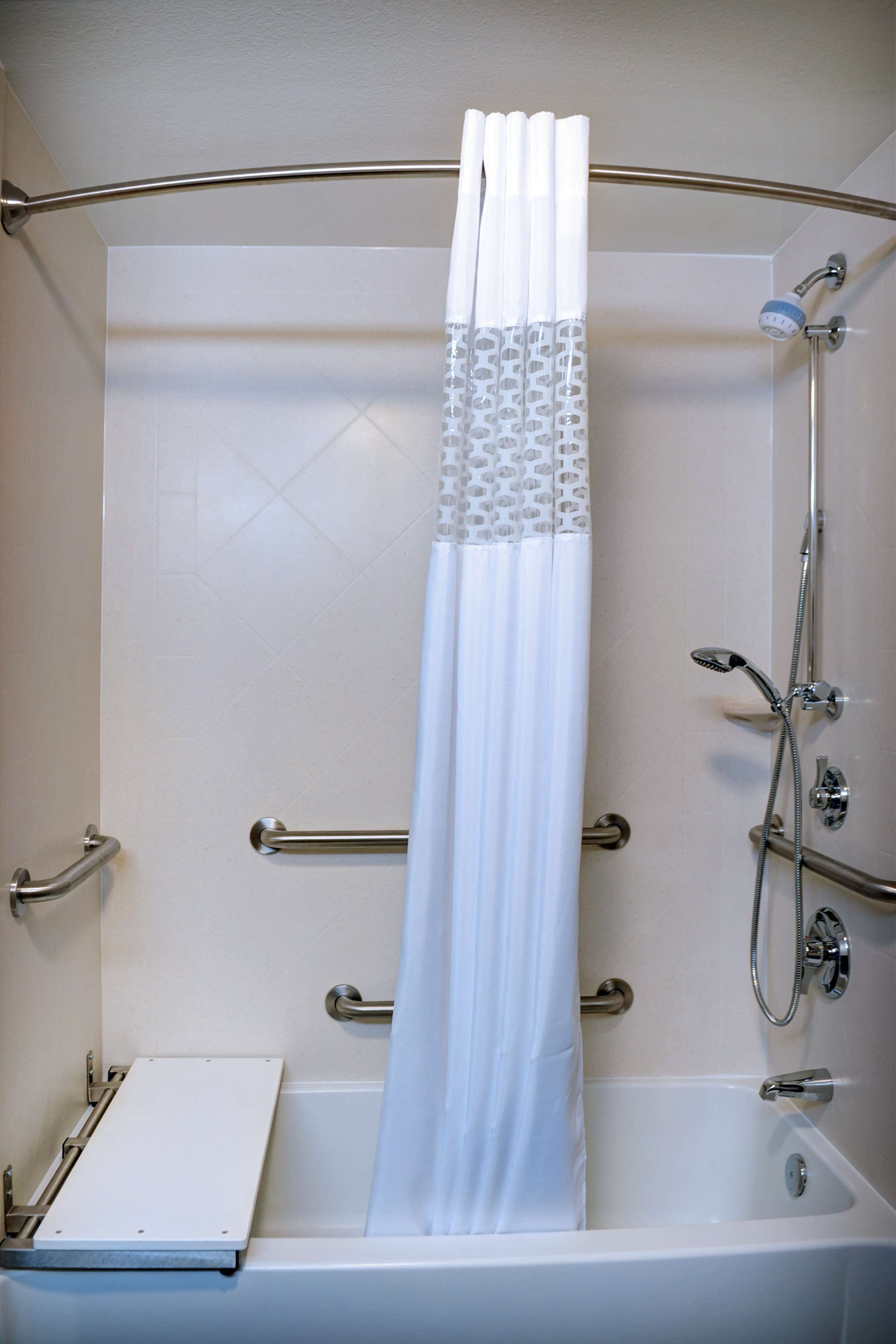 A shower area with a white curtain, grab bars, and a handheld showerhead.