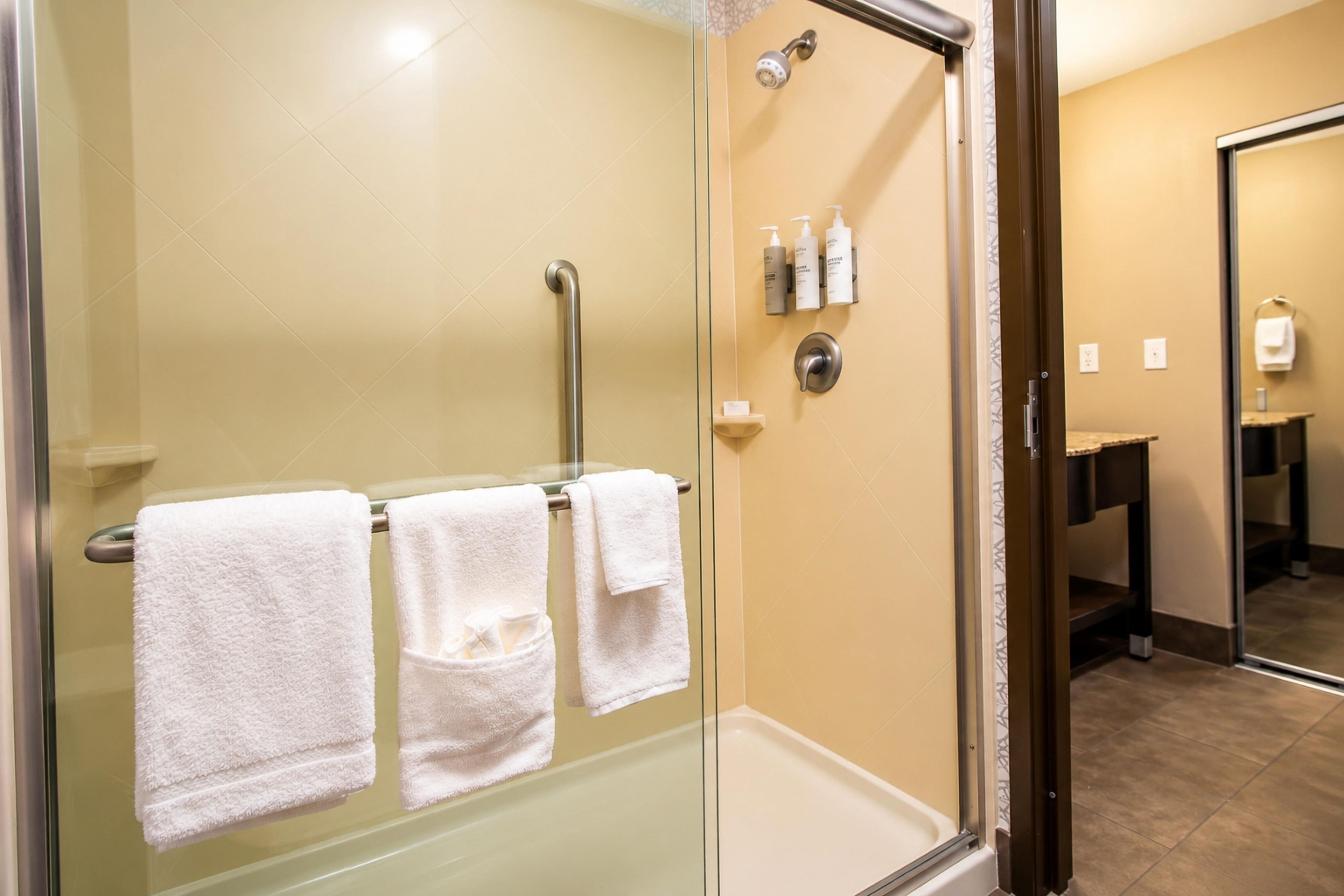 A glass-enclosed shower area with a handrail, two towels, and toiletries on a wall-mounted shelf.
