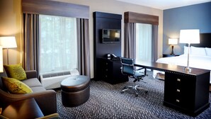A hotel room with a bed, a desk, a chair, a sofa, a TV, and a window with curtains.
