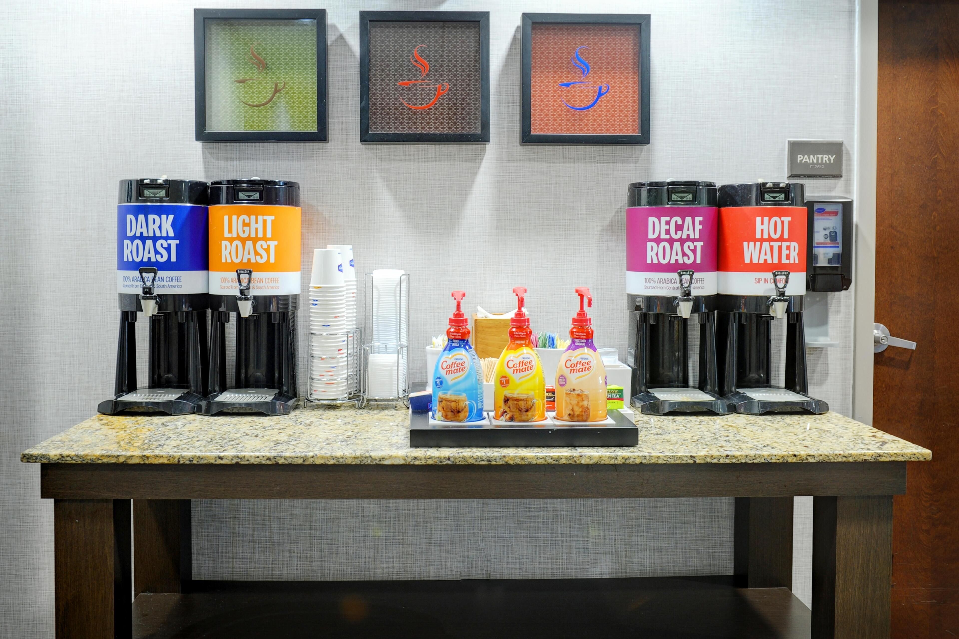 A coffee station with labeled dispensers for dark roast, light roast, decaf roast, and hot water.