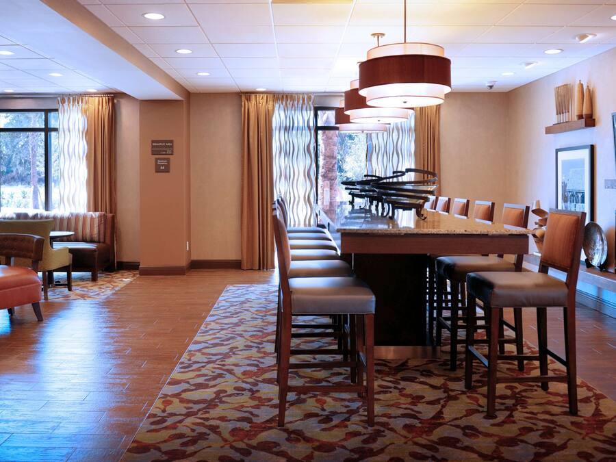 A hotel dining area with a long table, multiple chairs, a patterned rug, and a television on the wall.