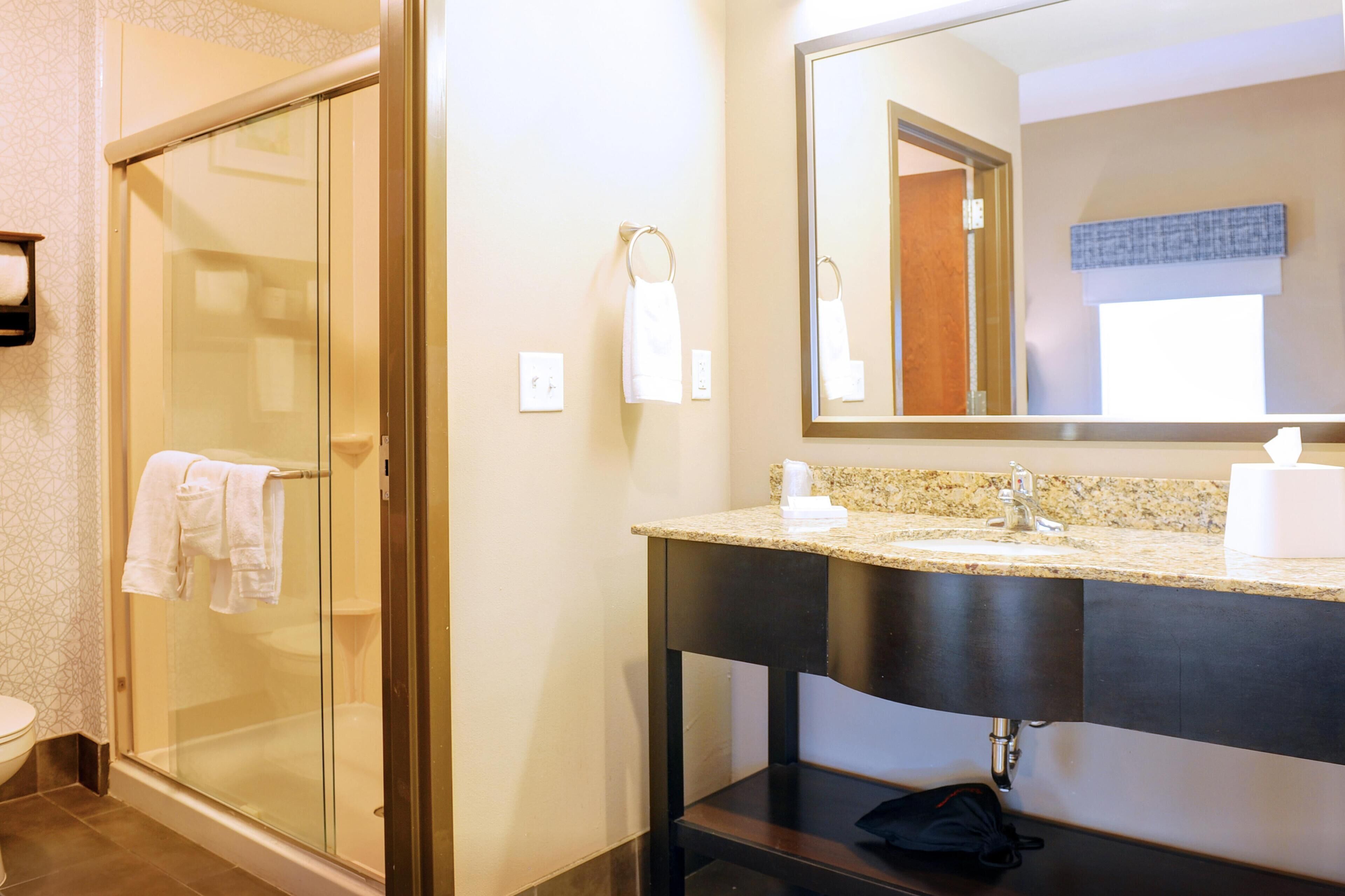 A bathroom with a glass shower enclosure, a sink with a towel dispenser, and a mirror above the sink.