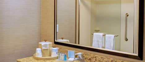 A hotel bathroom with a granite countertop sink, a large mirror, a towel rack, and a shower stall visible in the reflection.