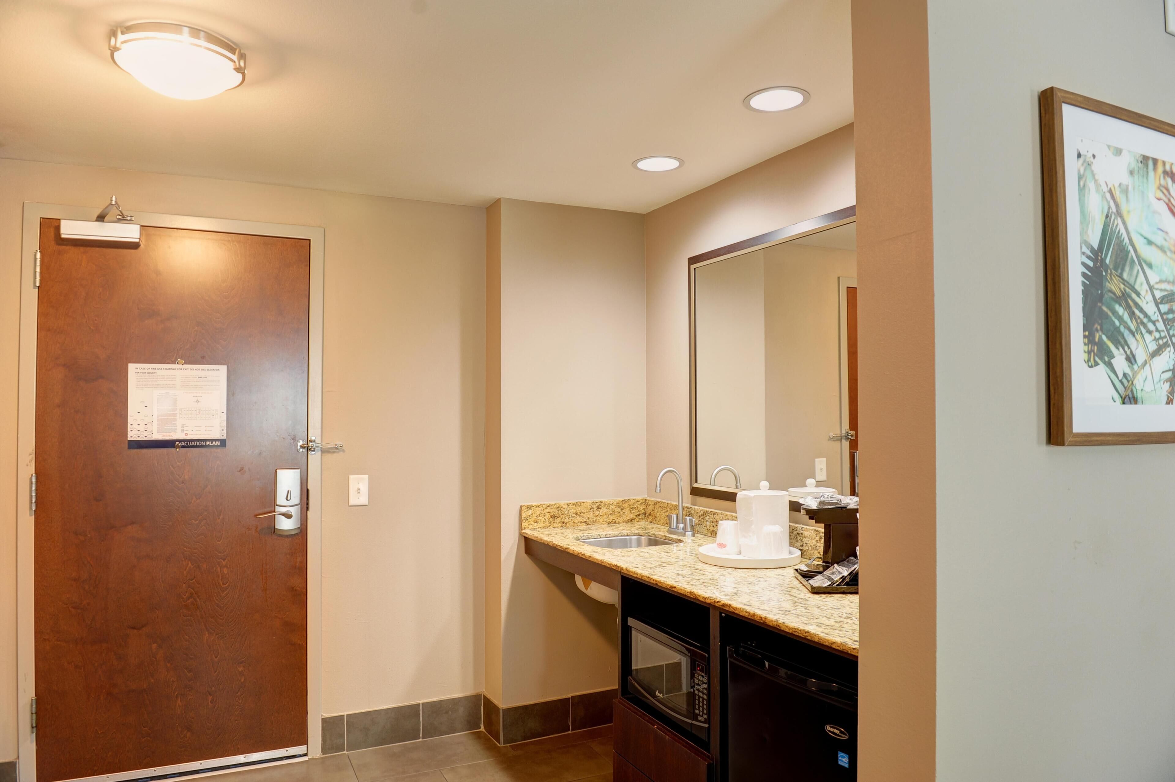 Une salle de bain d’hôtel avec une porte en bois, un lavabo doté d’un plan de travail en granit, un miroir et un four à micro-ondes.