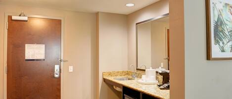 Une salle de bain d’hôtel avec une porte en bois, un lavabo doté d’un plan de travail en granit, un miroir et un four à micro-ondes.