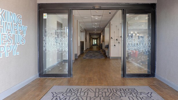 A hotel entrance with a glass door, a hallway leading to the interior, and a doormat with a motivational message.