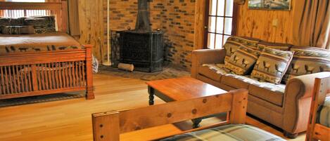 A cozy room with a wooden bed, a sofa with patterned cushions, a wooden table, and a brick fireplace.