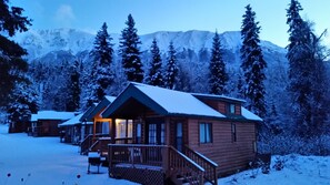 Une cabane dotée d’un porche, entourée d’arbres et de montagnes couverts de neige.