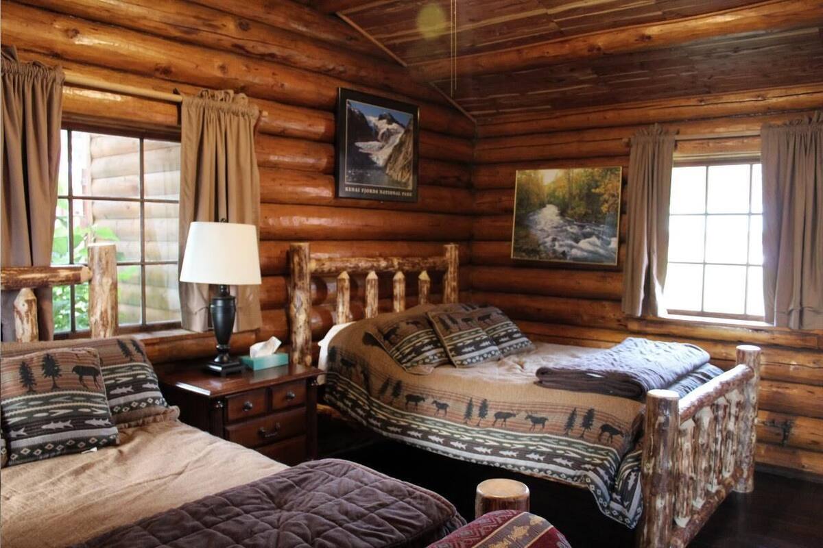 Une chambre dans un chalet en rondins, avec deux lits, une table de chevet, une lampe et un tableau représentant un paysage de montagne.