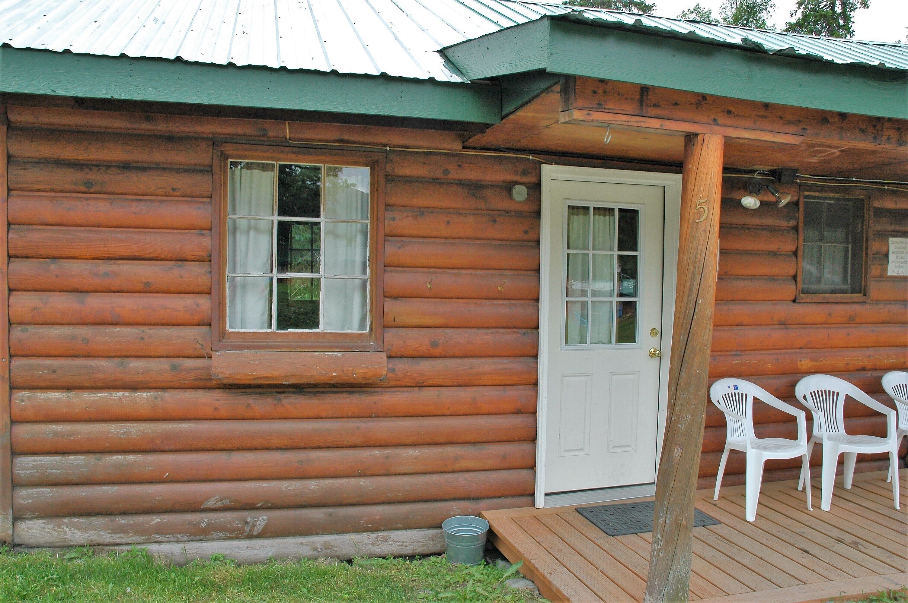 A log cabin with a wooden deck and two white plastic chairs.