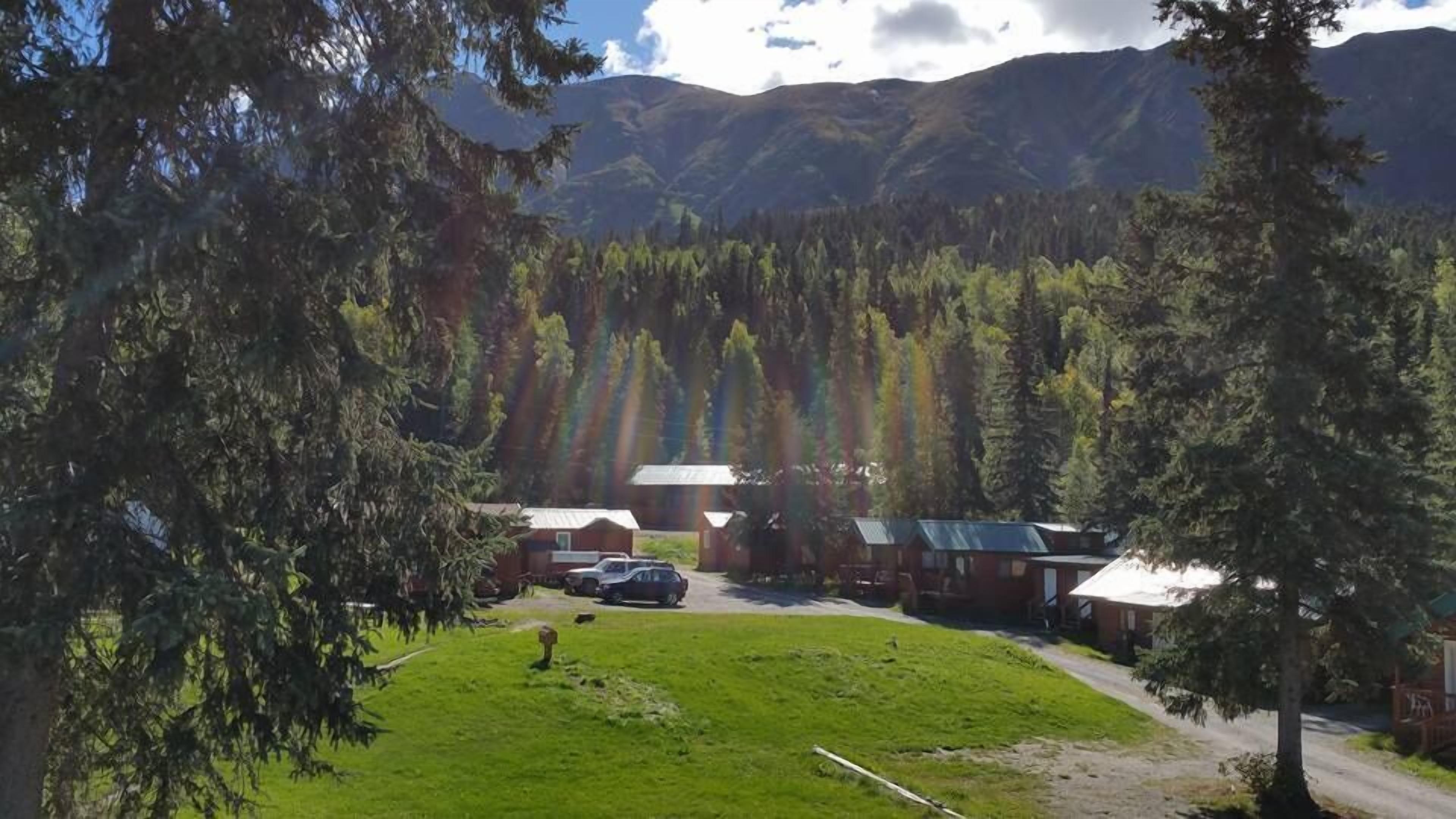 A lodge with cabins and a parking area surrounded by forest and mountains.