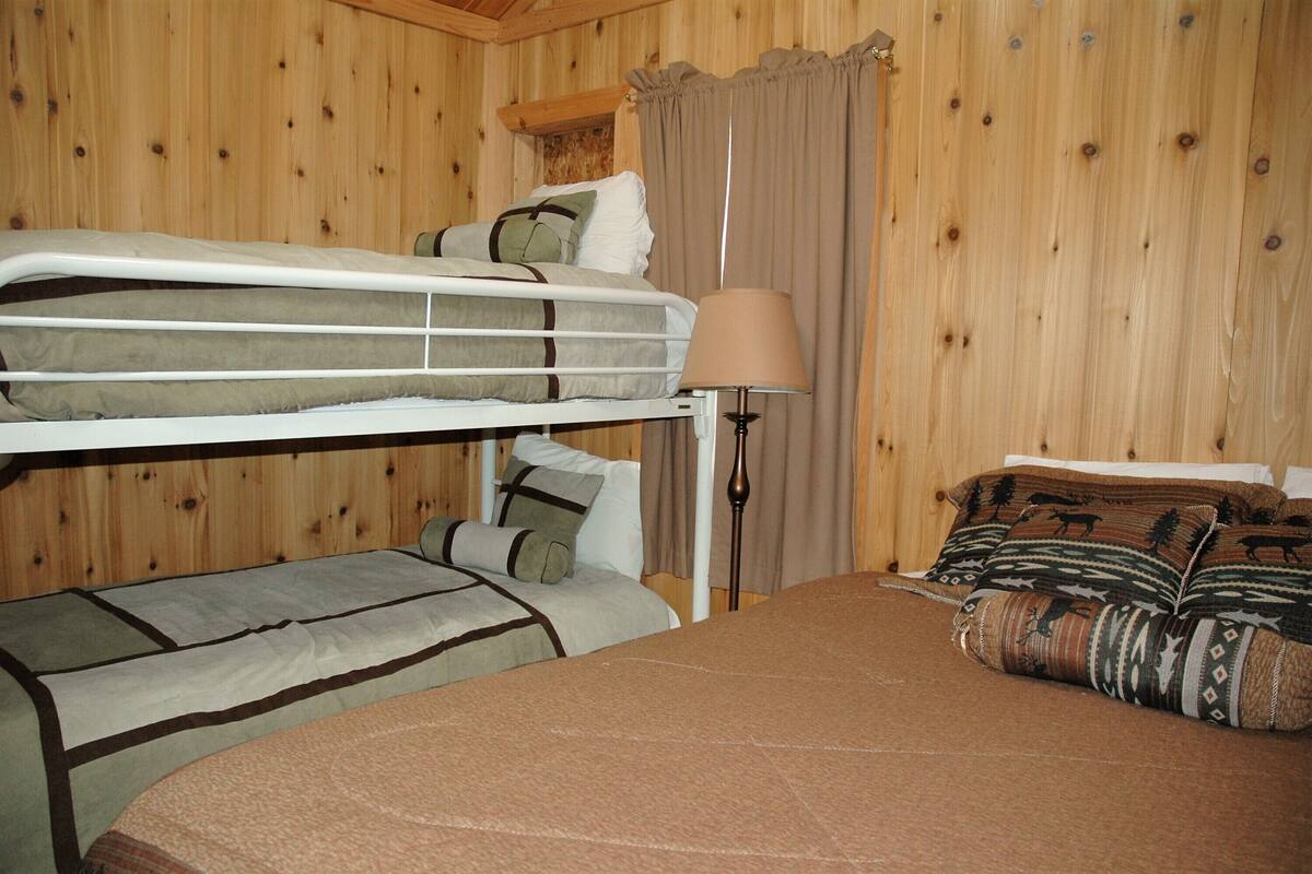 Une chambre avec un lit superposé, une table de chevet avec une lampe et un plaid à motifs.