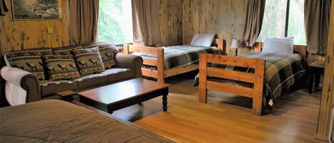 A cabin with two wooden beds, a sofa, a table, and a window with curtains.