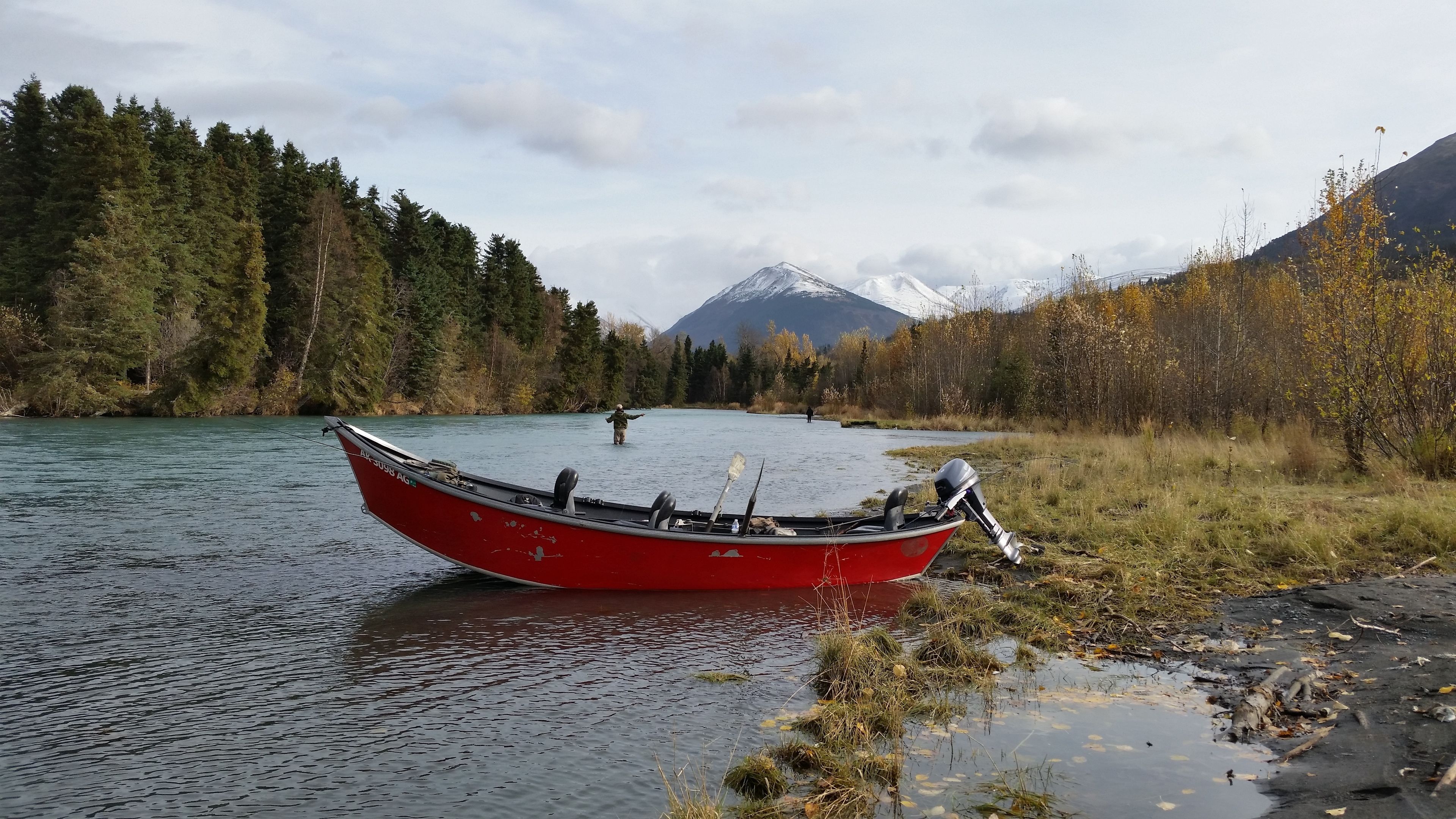 Een rode boot op een rivier, met een bos en bergen op de achtergrond.