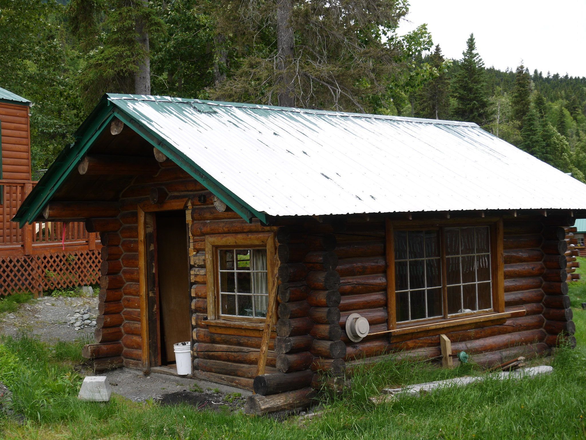 A rustic log cabin with a green roof, a wooden door, and a window with a grid pattern.