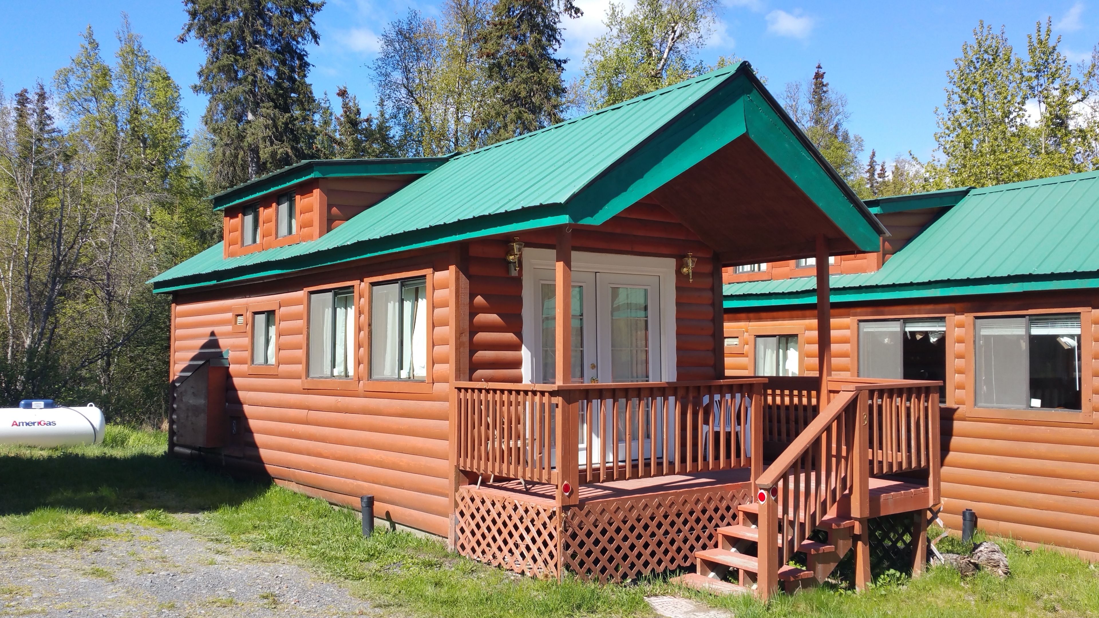 A wooden cabin with a green roof, a porch, and a small attached structure.