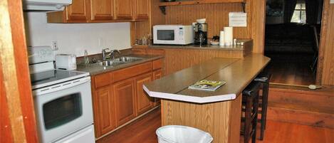 A kitchen with wooden cabinets, a microwave, a stove, and a trash can.