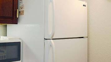 A kitchen with a white refrigerator, wooden cabinets, and a microwave.