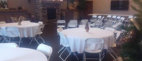 A conference room with round tables and white chairs, a fireplace, and a Christmas tree.