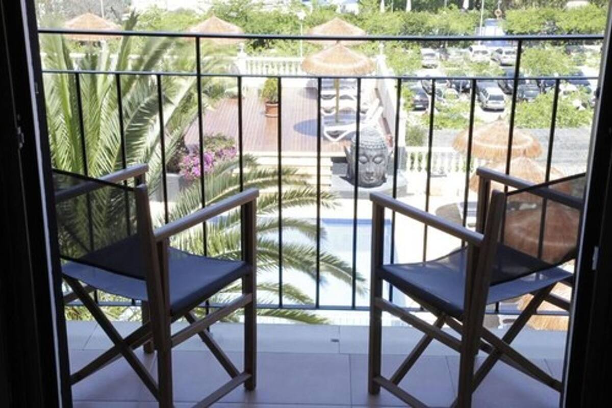 A balcony with two chairs, a Buddha statue, and a view of a parking area with cars and greenery.