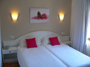 Uma cama de casal com duas almofadas cor-de-rosa, cabeceira branca e um quadro pendurado na parede com pedras e flores.