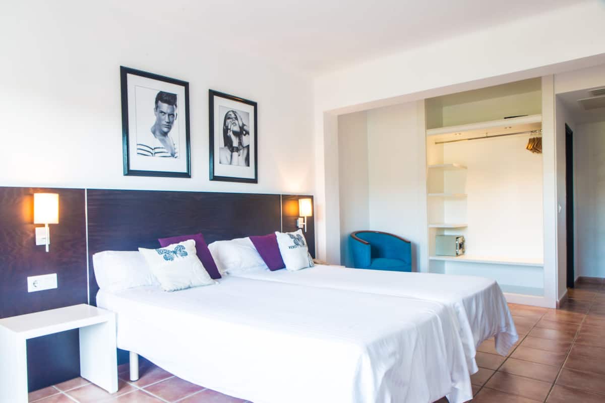 A hotel room with a large bed, two bedside tables, a wardrobe, and a bathroom visible through an open door.