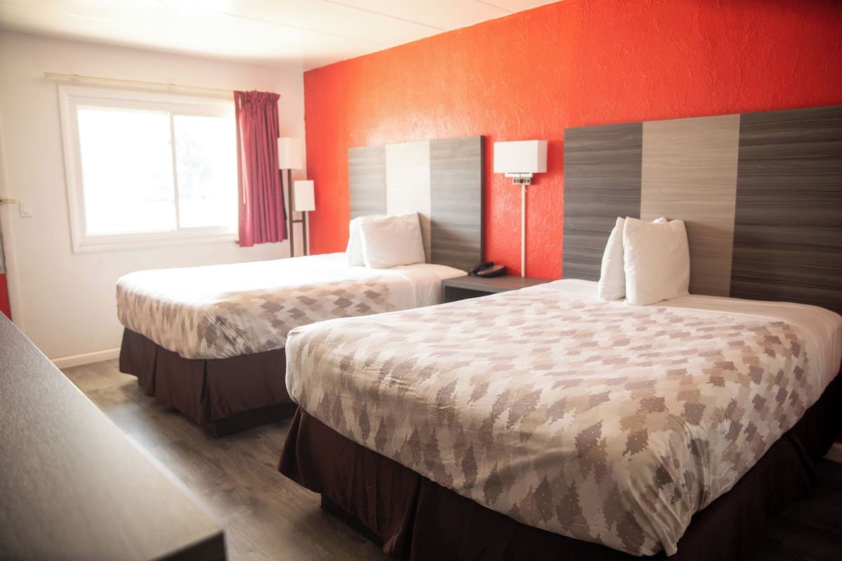 A hotel room with two beds, a window with curtains, bedside lamps, and a red accent wall.