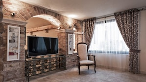 A living room with a TV on a glass cabinet, a chair, and a brick wall. - Hotel Azimut (Sveti Stefan)