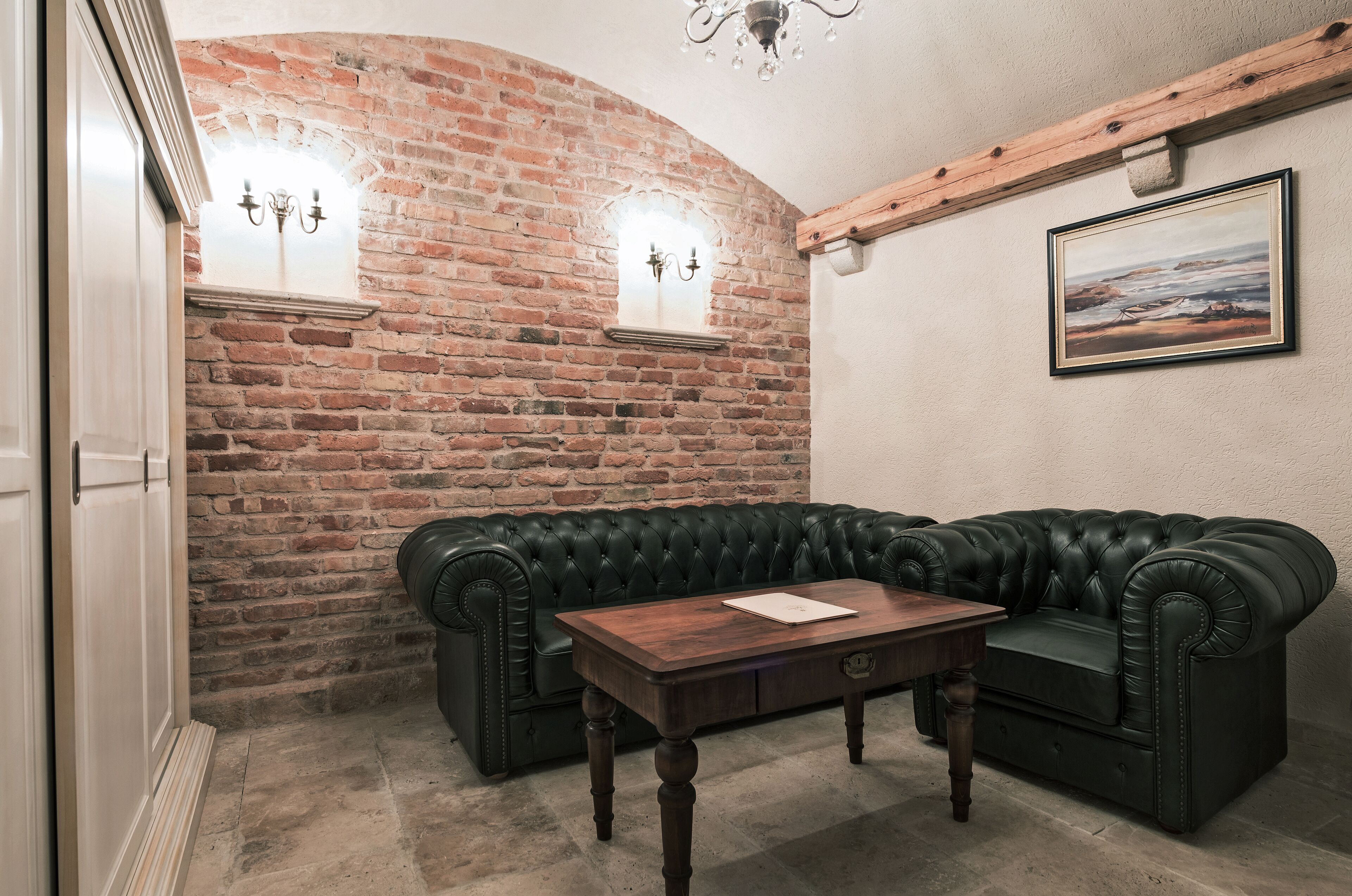 Una habitación con pared de ladrillo, sofá de cuero negro, mesa de centro de madera y un cuadro en la pared.