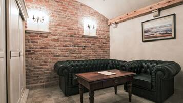 Una habitación con pared de ladrillo, sofá de cuero negro, mesa de centro de madera y un cuadro en la pared.