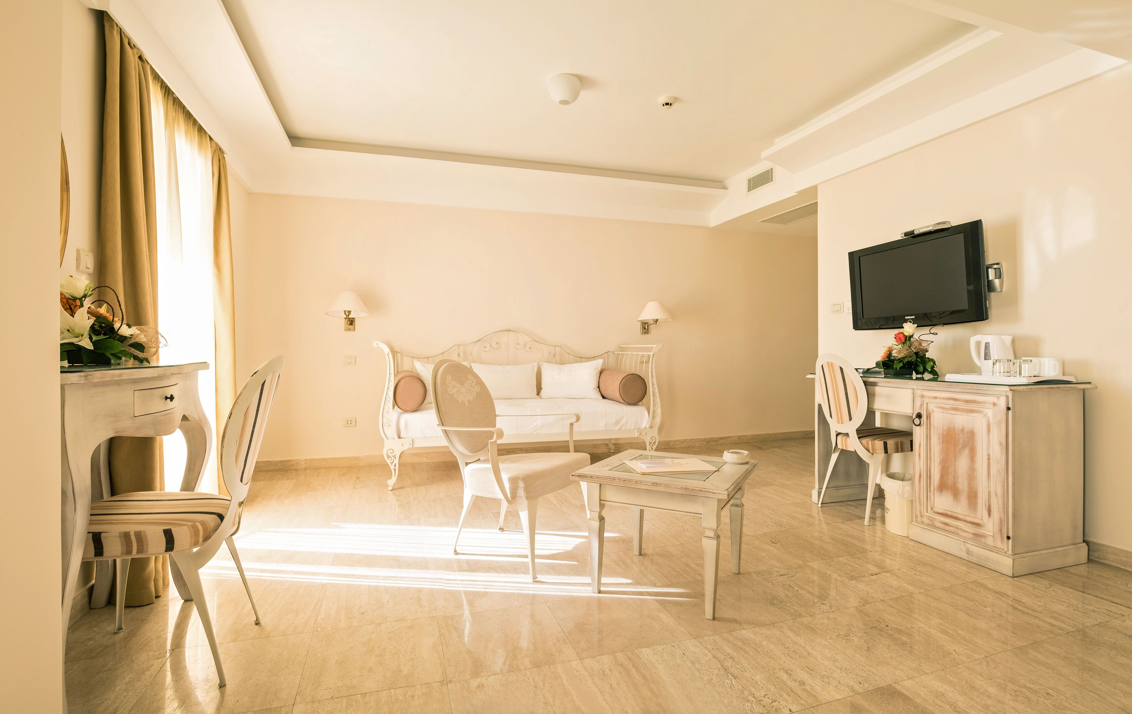 Quarto de hotel com uma cama, duas cadeiras, uma mesa, uma televisão e um armário.