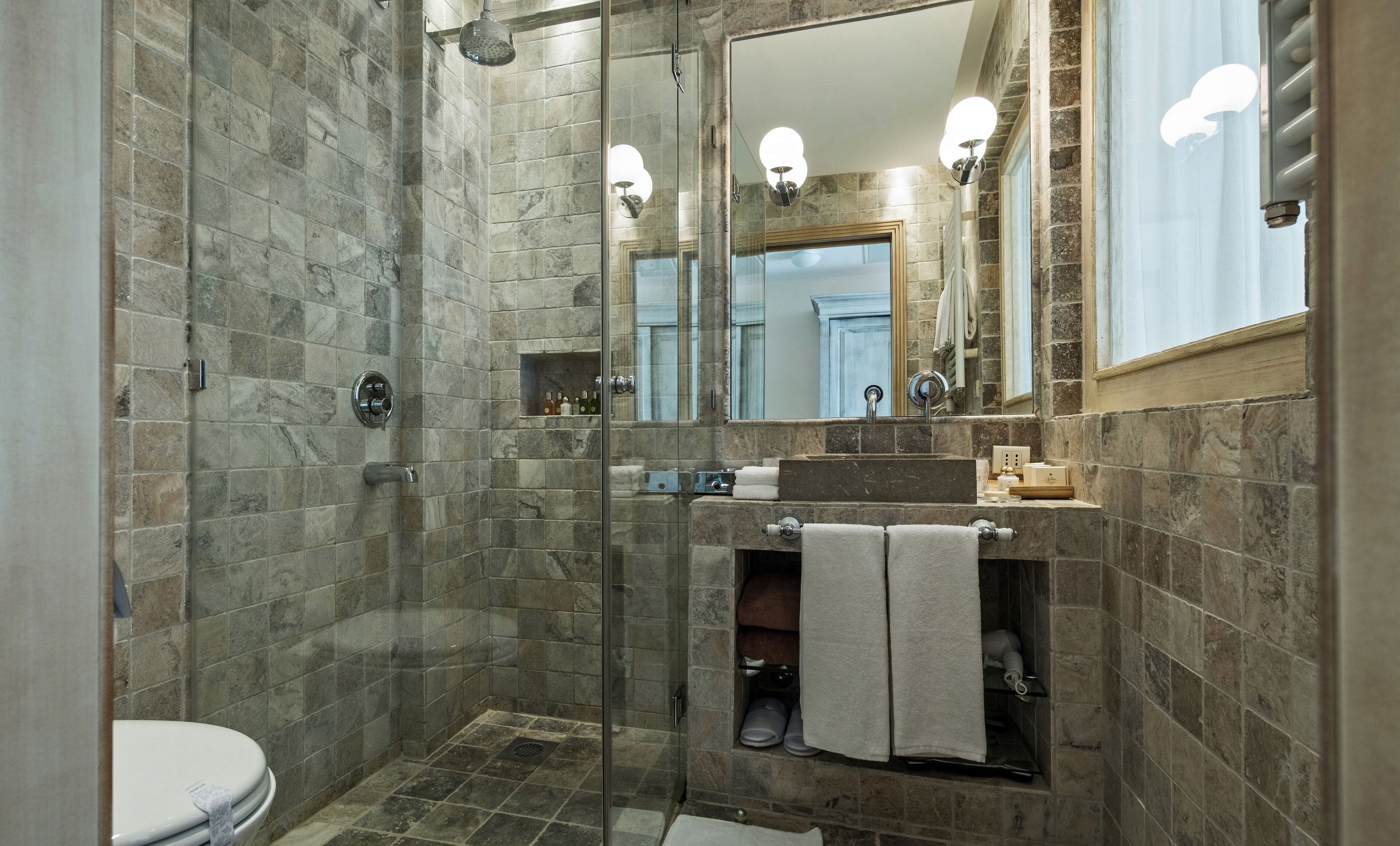 Een moderne badkamer met een douchecabine van glas, een wastafel met spiegel erboven en een toilet.