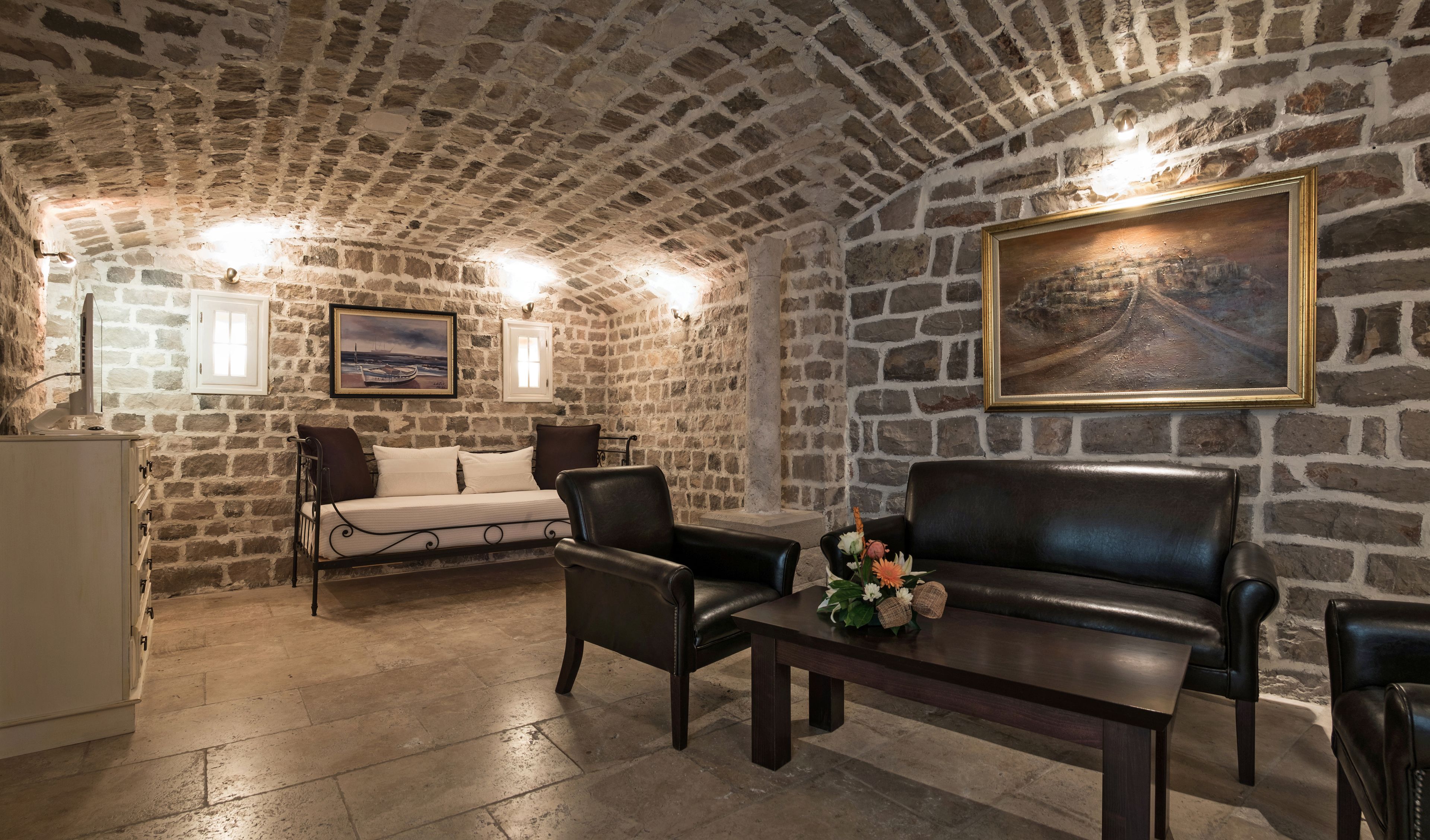 Una habitación con paredes de piedra, un sofá, dos sillas, una mesa con flores y un cuadro en la pared.