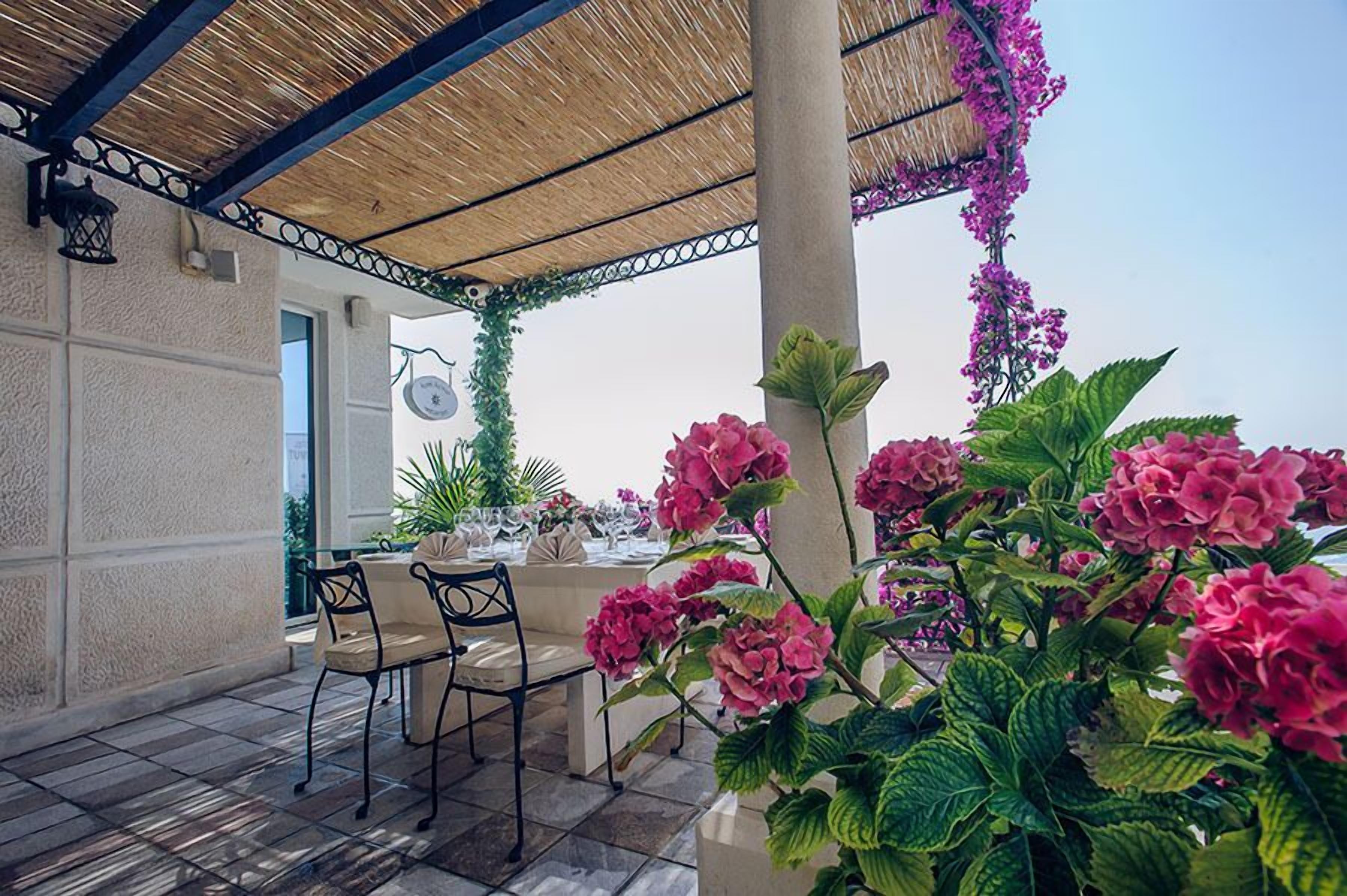 An outdoor dining area with a covered patio, tables set for dining, and lush greenery.