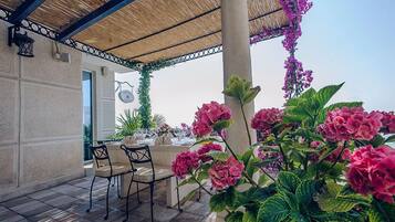 An outdoor dining area with a covered patio, tables set for dining, and lush greenery.