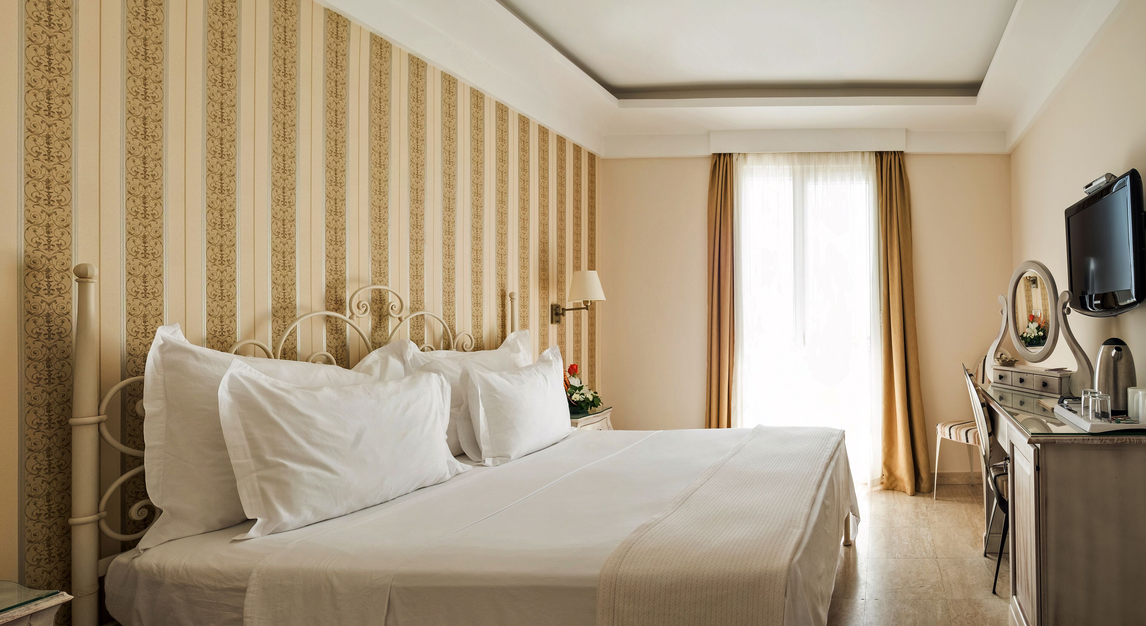 Una habitación de hotel con una cama grande, un escritorio con espejo y un televisor en la pared.