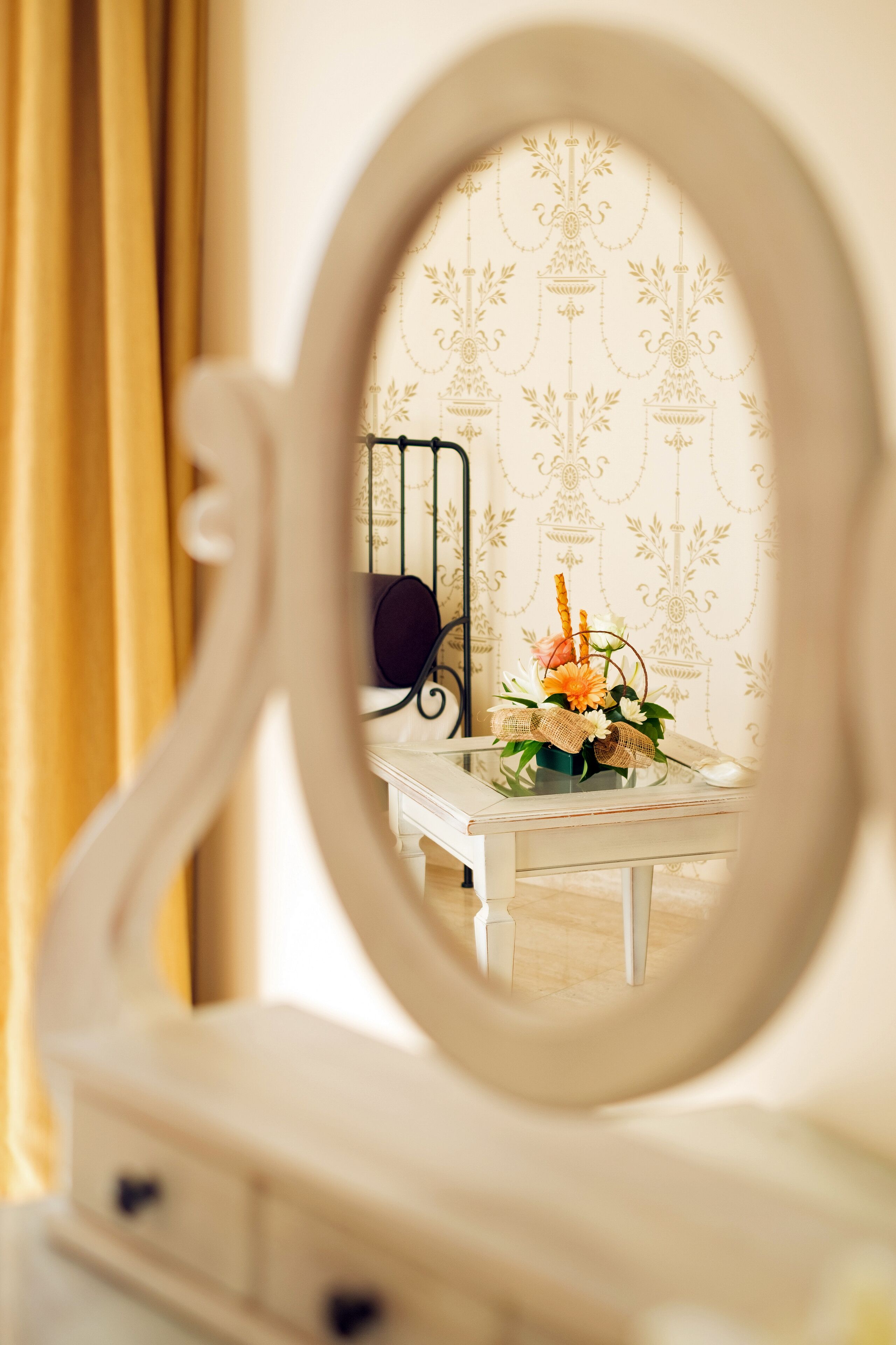 A mirror reflecting a room with a bed, a dresser, and a vase with flowers.