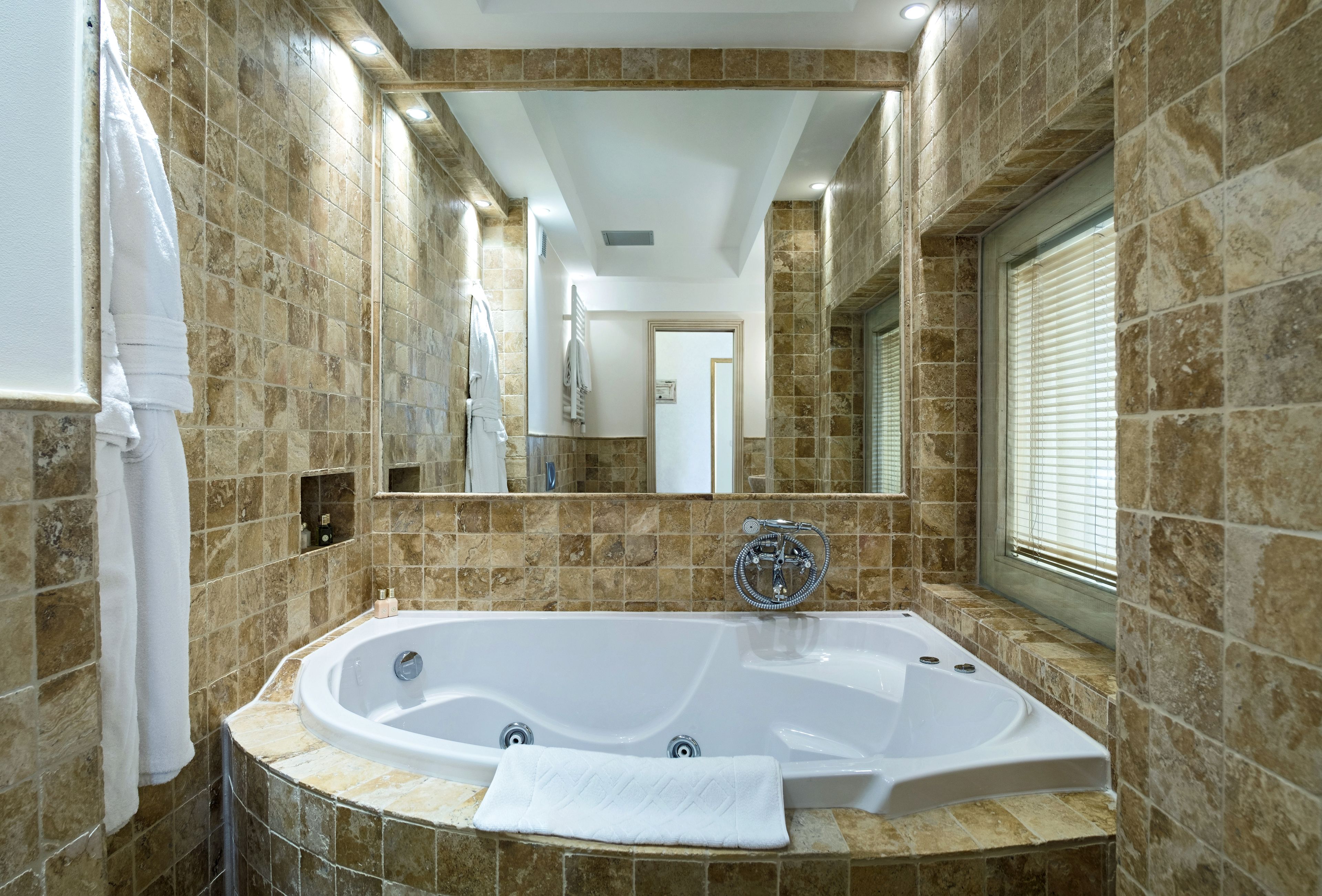 A modern bathroom with a freestanding bathtub, a large mirror, and a window with blinds.